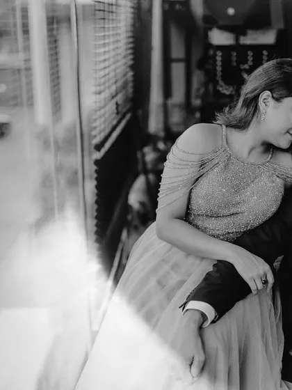 A black and white photo capturing a quiet moment by a large window. The reflection and soft light add an artistic and introspective feel to this urban pre-wedding portrait.