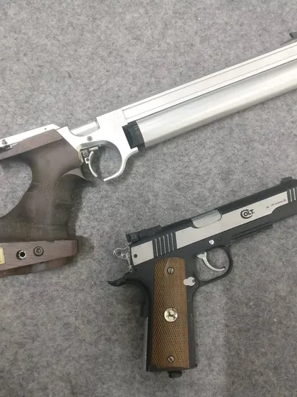 A competition air pistol and a .22 caliber Colt pistol side by side. We offer training in various categories, from the 10m air pistol Olympic event to other firearm shooting experiences.