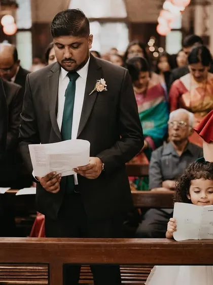 A young girl stands on a church pew, intently reading the ceremony leaflet alongside the adults. This charming photo captures a child's earnest attempt to participate in the grown-up world.