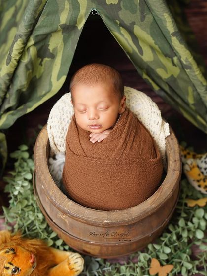 A little explorer in his jungle camp. This newborn is swaddled and sleeping in a basket, tucked inside a camouflage tent.
