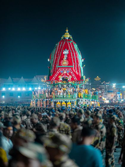 The sacred chariot of Lord Jagannath seen at night, surrounded by security forces and a sea of devotees. The atmosphere is electric.