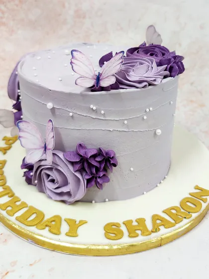 A side view of the purple butterfly cake, showing the textured frosting and the arrangement of flowers.