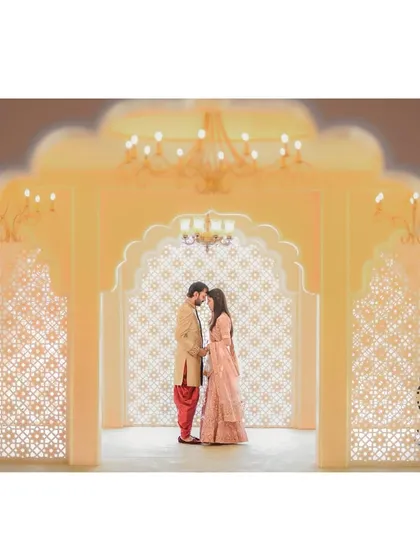 A stunning wide shot of the couple framed by an ornate Rajasthani-style archway, lit beautifully to create a warm, golden glow.
