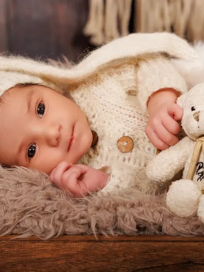 Wide awake and curious, this newborn cuddles with a teddy bear in a rustic wooden bed prop, showing that awake shots can be just as precious.