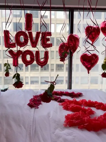 A closer look at the details of my romantic room setup. You can see the 'I LOVE YOU' foil balloons, heart-shaped balloons, and delicate roses hanging with the ribbons, all set against a city view.