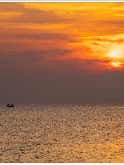 A lone fishing boat sails on the calm sea under a fiery sunset in the Andaman Islands. This is a simple, minimalist composition that evokes a sense of peace.