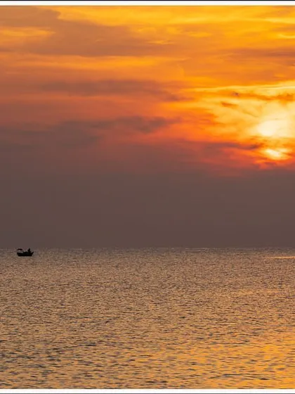 A lone fishing boat sails on the calm sea under a fiery sunset in the Andaman Islands. This is a simple, minimalist composition that evokes a sense of peace.