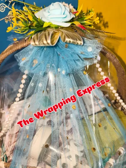 A closer look at the wrapped baby hamper, showing the pearl string detail and the blue rose decoration.