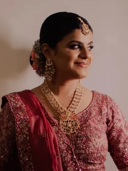 A radiant bride smiling, captured in soft, glowing light. Her look features a traditional floral bun and timeless gold jewelry, perfect for her wedding ceremony.