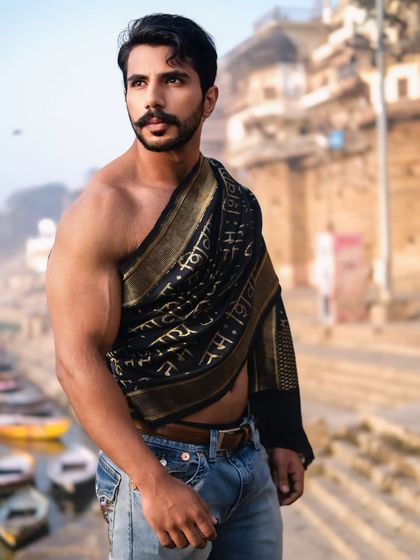 A close-up portrait capturing a strong gaze and the intricate details of the 'Om Namah Shivaya' drape, set against the soft focus of the ghats.