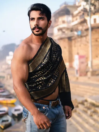 A close-up portrait capturing a strong gaze and the intricate details of the 'Om Namah Shivaya' drape, set against the soft focus of the ghats.