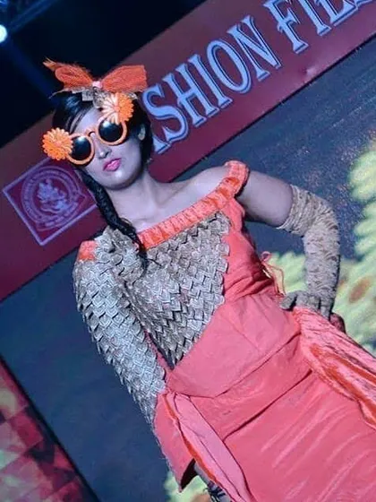 This runway look highlights creative accessorizing and fabric texturing. The student designer created a woven bodice and paired it with a flowing orange skirt and custom-made, whimsical sunglasses.