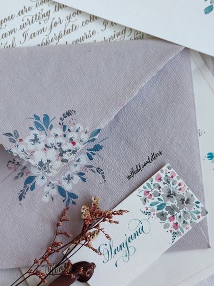 A close-up of one of the hand-painted envelopes from the gratitude series, featuring a beautiful spray of white and blue florals on a dusty lavender envelope.
