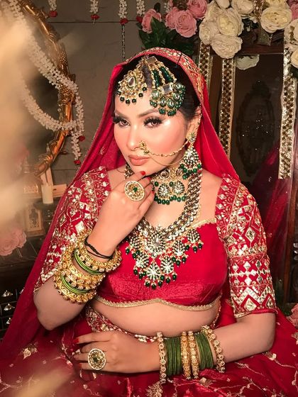A portrait of my classic bride. The makeup features a flawless base, smoky eyes, and is perfectly coordinated with the red lehenga and green kundan jewelry.