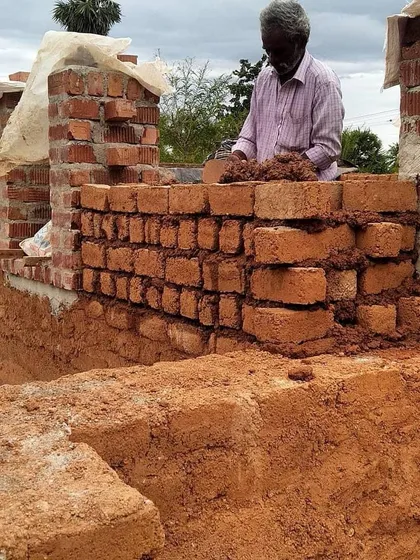 A local mason building up a wall with adobe bricks and mud mortar. We prioritize training and employing local craftspeople, empowering the community and ensuring the skills of natural building are passed on.