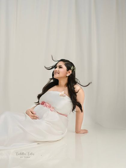 A portrait of pure joy. The wind in her hair and the soft white dress create a feeling of freedom and happiness. This is a celebration of the beautiful journey of motherhood.