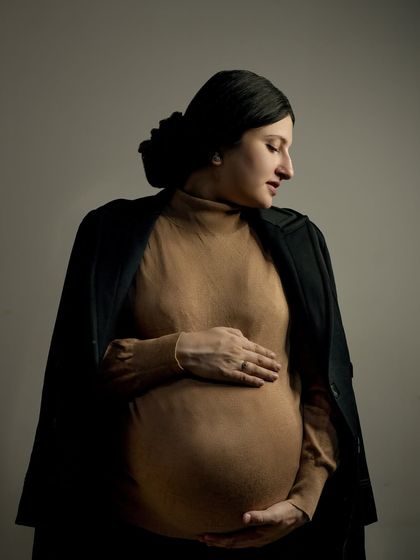 A classic and elegant maternity portrait. The simple, focused lighting highlights the beautiful silhouette of the baby bump, creating a timeless piece of art that you will cherish forever.