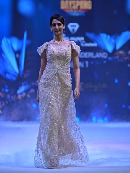 This golden gown, fully adorned with Swarovski stones, features an elegant off-shoulder neckline and a cinched waist, creating a timeless and sophisticated silhouette.