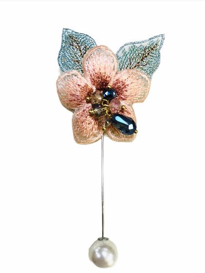 A delicate lapel pin featuring an embroidered pink flower with beaded details and a single pearl drop. This piece adds a soft, feminine touch to blazers, dresses, or coats.