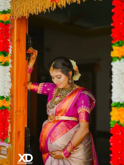 A beautiful portrait of the mother-to-be looking down at her baby bump, framed by colorful flower garlands at her baby shower.