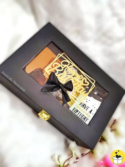 The closed view of a luxe hamper for men. The elegant black box with a clear window and a beautiful bow promises something special is waiting inside.