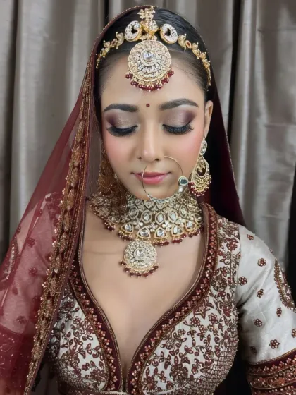 A close-up of a bride with stunning smokey eye makeup and a neutral lip, creating a modern and glamorous look with her traditional maroon and white lehenga.