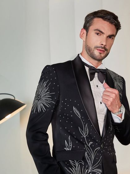 A detailed shot of the embroidered black ceremonial suit. The silver threadwork catches the light, showcasing the artistry and making it a standout piece for any groom or wedding guest.