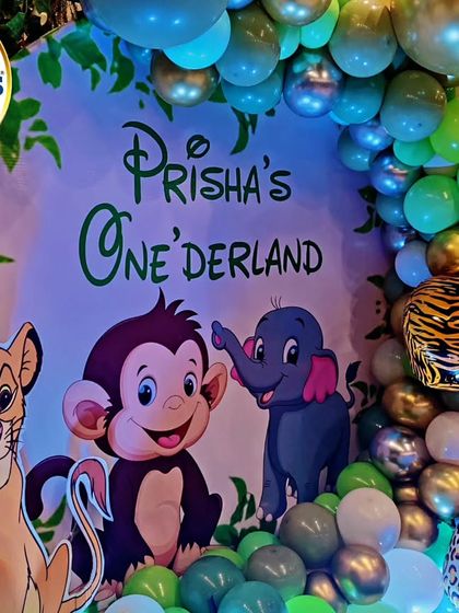 A close-up of our jungle-themed 'Onederland' backdrop. This shot highlights the custom-printed background featuring characters like Simba, Dumbo, and a monkey, surrounded by a green and metallic balloon arch.