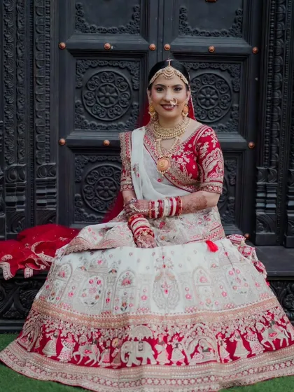 A beautiful full-length portrait of the bride against an ornate door. Her makeup and lehenga create a look of pure royalty, with every detail from her matha patti to her embroidered skirt perfectly harmonized.