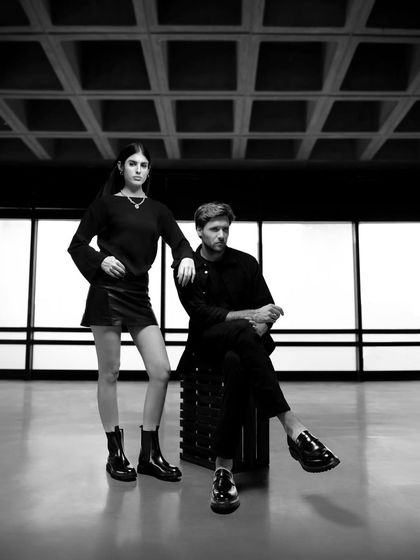 A black and white campaign image for Moral Code. The styling is all-black, creating a chic, powerful look that puts the focus on the models' confident poses and the brand's accessories.