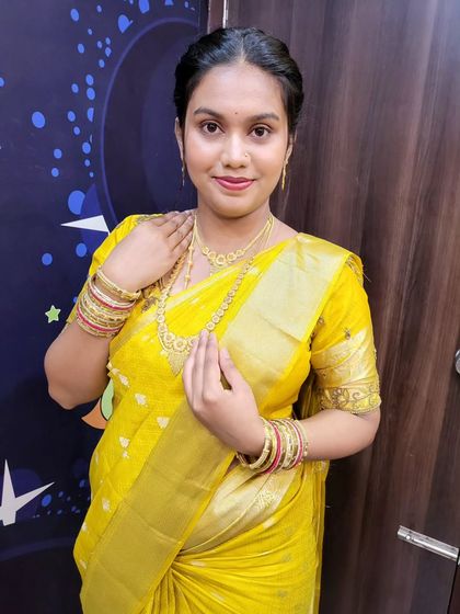 The client looks radiant in her gold saree. The draping is done to complement her simple jewelry and hairstyle, creating a cohesive and graceful look.