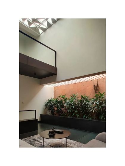 A multi-level view of the Notan Home, where a bridge overlooks a sitting area with an indoor planter. The design emphasizes vertical connection and the integration of natural elements.