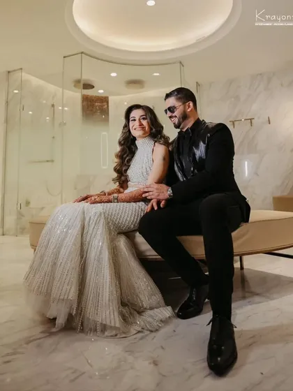 A stylish portrait of the couple, seated in a modern, marble-clad setting. Their reception look is the epitome of contemporary chic.