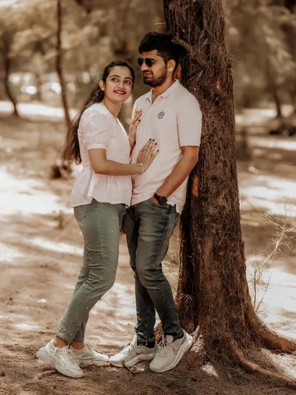 A playful and romantic moment as a couple poses by a tree in a sun-dappled forest.
