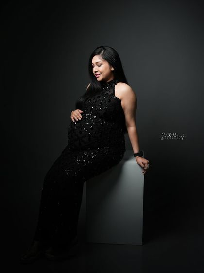 A serene portrait of a mother-to-be seated in a black sequined gown. The dramatic lighting and her peaceful expression create a moment of quiet elegance.