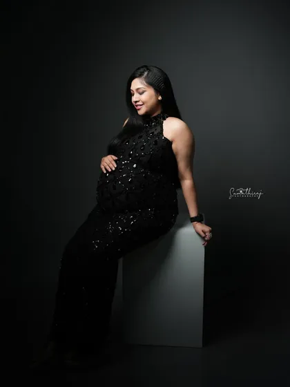 A serene portrait of a mother-to-be seated in a black sequined gown. The dramatic lighting and her peaceful expression create a moment of quiet elegance.