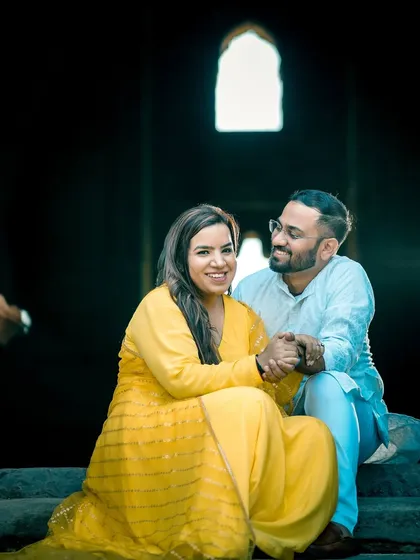 A relaxed portrait of the couple holding hands. The contrast between the dark interior and the bright light from the arched window creates a beautiful, classic composition.