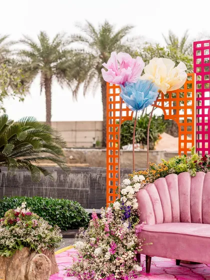 A pink scalloped sofa surrounded by flowers, with oversized paper flowers and colorful lattice screens in the background.