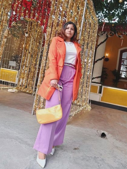 Posing against festive lights, this colorful outfit shines even brighter. The orange and purple pairing is a great example of how to use the color wheel to create visually exciting and harmonious looks.