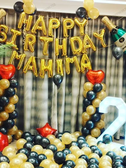 A birthday surprise decoration in a living room. This setup includes 'Happy Birthday' foil letters, balloon pillars with champagne bottle foils, and a light-up marquee number '26'.