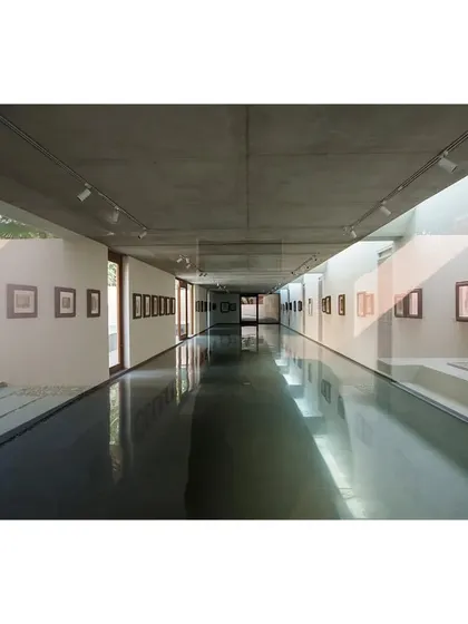 The long, linear expanse of the subterranean gallery at the Kasturbhai Lalbhai Museum. The polished black floor reflects the artwork and the light from the side courtyard, creating a sense of infinite space.