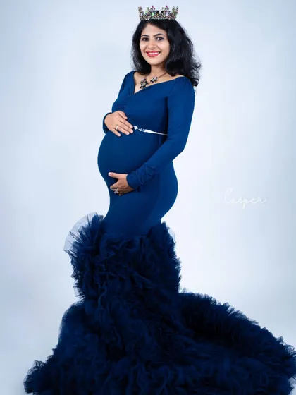 A full-length portrait in a navy blue mermaid gown with a dramatic ruffled train. The simple white background makes the color and style of the dress pop.