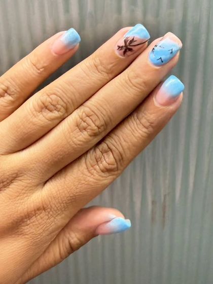 Another angle of the beach-themed nails, showing the palm tree and bird details on a soft blue gradient.