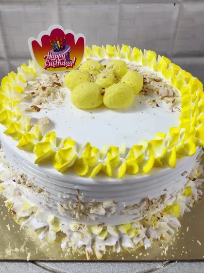 A birthday cake with a fusion twist, topped with rasmalai pieces and chopped nuts.