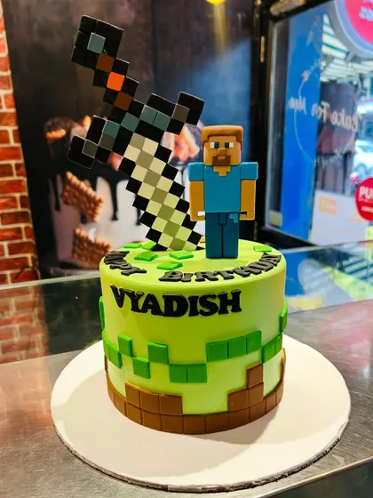 A Minecraft-themed cake with pixelated fondant blocks, a character figurine, and a giant pixel sword topper.