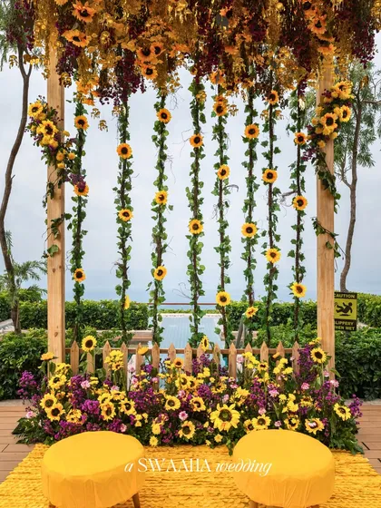 A creative photo backdrop made of a wooden frame with hanging sunflower garlands, set against a poolside view.