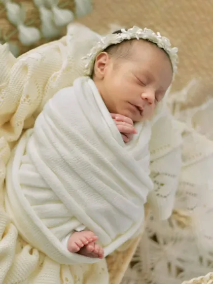 Wrapped in a textured white blanket with a delicate floral headband, this newborn is the picture of serenity. This image showcases a clean, boho-inspired aesthetic.