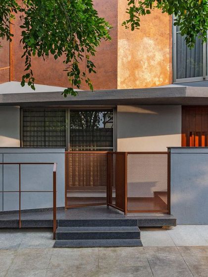 The entrance to the Copper House features a layered composition of materials. A perforated copper gate and screen provide security and privacy while allowing light and air to pass through, set against a backdrop of textured plaster and smooth concrete.