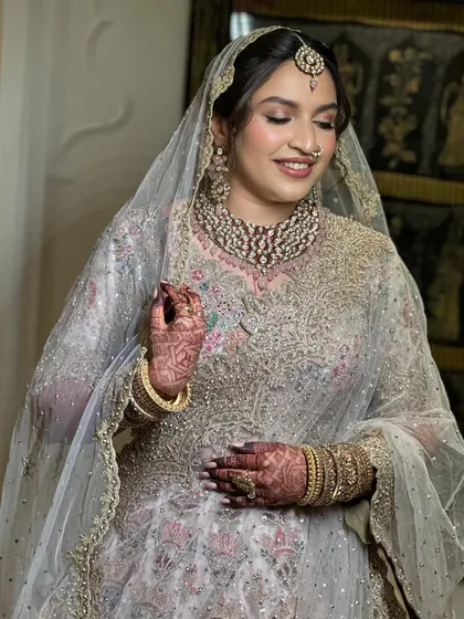 A lovely bride smiling, with her hair styled in a soft, low updo beneath a delicate net veil. This look is perfect for a Nikah or reception, offering a touch of modern elegance.