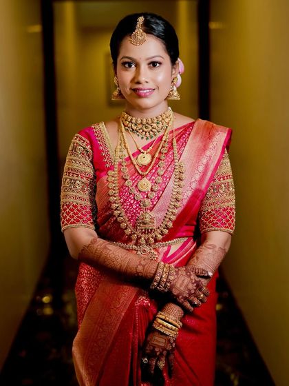 A full-length portrait of Lavanya, showcasing her complete bridal look with intricate gold jewelry and a radiant smile.